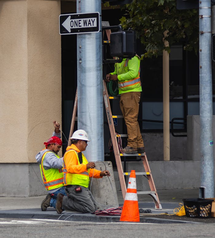 hero-img-02 City workers in reflective gear maintain and repair a traffic signal on a bustling urban street.
