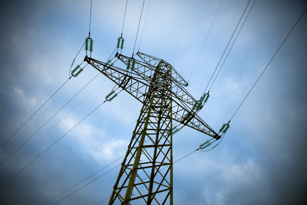 gallery-5 A majestic transmission tower stands tall against a cloudy blue sky, showcasing modern electric infrastructure.