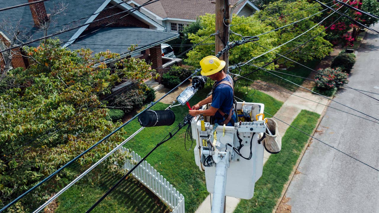 gallery-2 Electrician in a bucket lift repairing power lines from a utility pole in a suburban neighborhood.