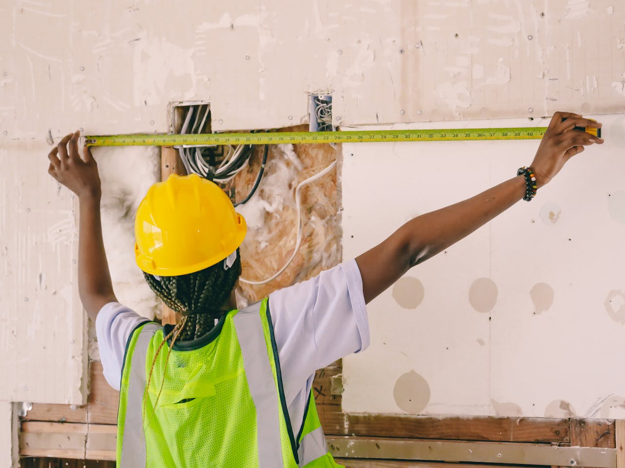 our-services-1 Female construction worker with hardhat and vest measuring an interior wall.