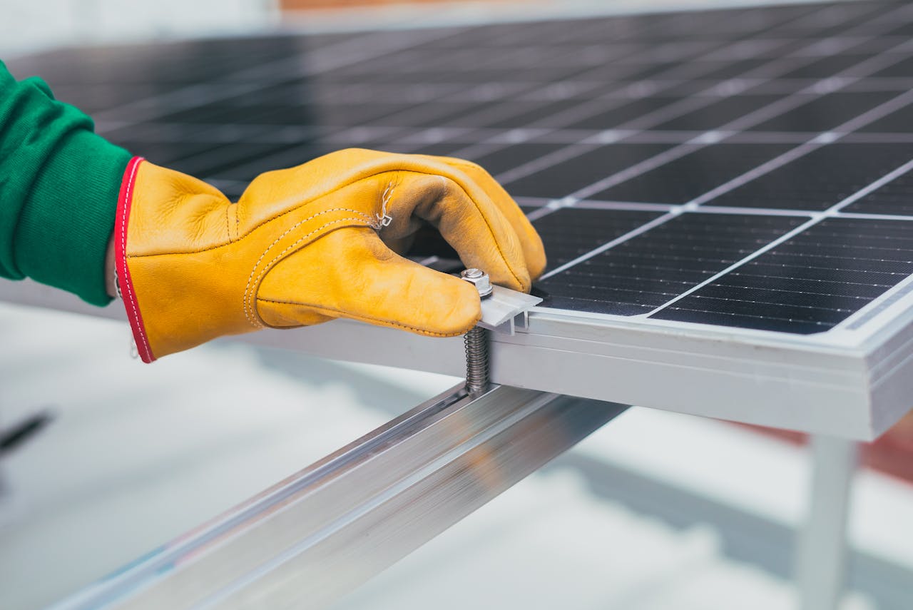 services-02 Close-up of a worker's hand with protective gloves adjusting a bolt on a solar panel.